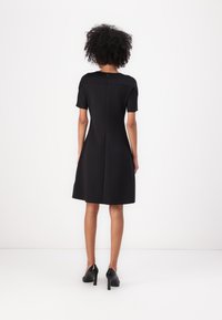 Rochie neagră în forma literei A, cu mâneci scurte, dintr-un material structurat și cu un fermoar discret la spate. Asortată cu încălțăminte cu toc înalt, de design minimal.