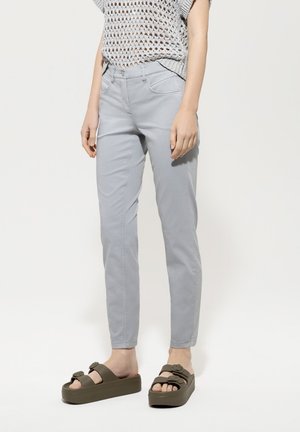 Light grey, slim-fit pants with front pockets, paired with olive green platform sandals featuring two straps and round buckles.