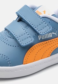 Zapatilla ligera azul con logo naranja de Puma, dos correas de Velcro, textura de cuero, suela blanca y forro de malla azul.