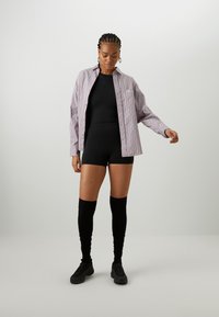 Black fitted bodysuit, oversized striped button-up shirt in white and lavender, knee-high black socks, and black slip-on shoes.