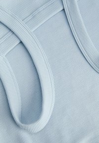 Lyseblåt ribbet stof med close-up af to overlappende buede stropper med syede kanter.