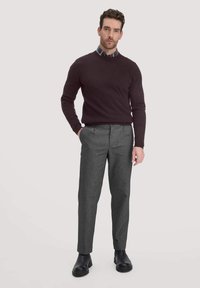 Dunkelmaroones Herrenpullover mit Rundhalsausschnitt, kombiniert mit grauen, maßgeschneiderten Hosen. Schwarze Knöchelstiefel ergänzen das Outfit. Ein karierter Hemd ist darunter sichtbar.