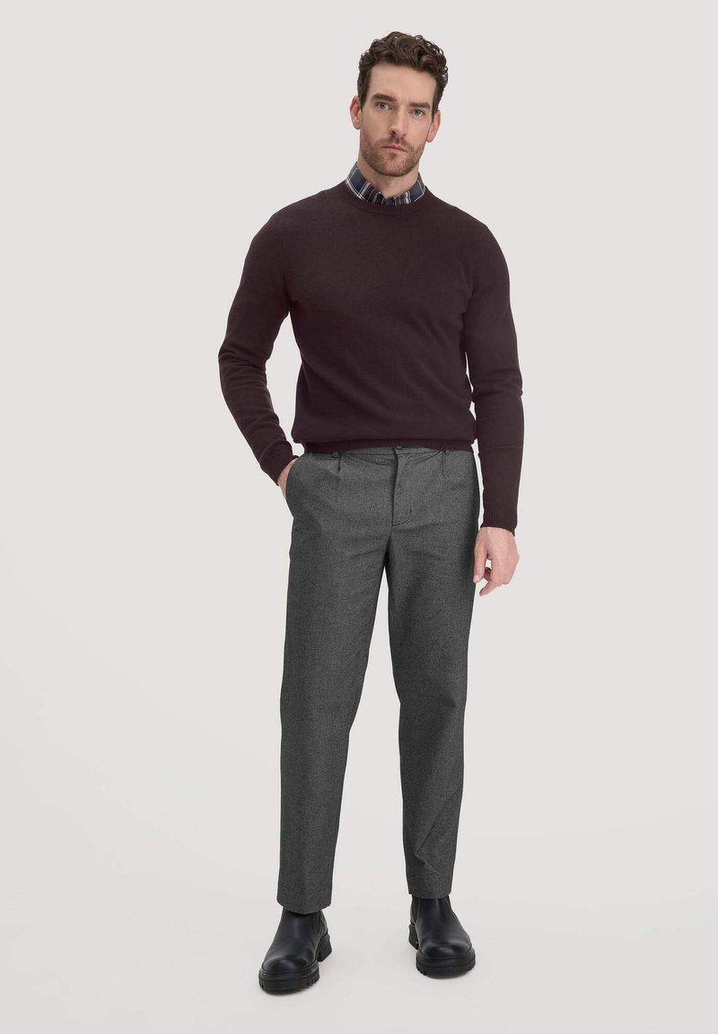 Donker bordeauxrood sweater voor heren, met ronde hals, gecombineerd met grijze op maat gemaakte broek. Zwarte enkellaarzen maken de outfit compleet. Geruit overhemd zichtbaar eronder.