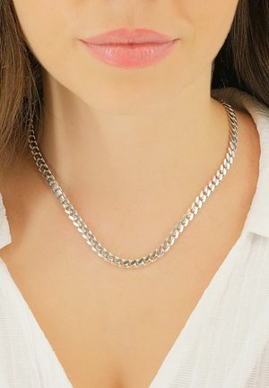 Collana in argento con design a doppio filo e maglie appiattite, che riflettono la luce. Lo sfondo è neutro con una camicia bianca dalla texture.