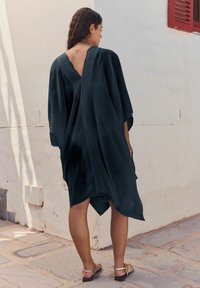 Musta, kevyt kimono-tyylinen mekko, jossa on V-mallinen selkäosa, virtaavat hihat ja epäsymmetrinen helma. Pehmeä materiaali, sopii lämpimiin sääolosuhteisiin.