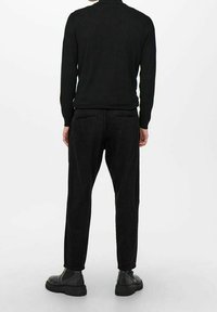 Zwarte corduroy broek met een ontspannen pasvorm, voorzien van achterzakken en een gestructureerde afwerking. Gecombineerd met zwarte schoenen en een getailleerd zwart sweater.