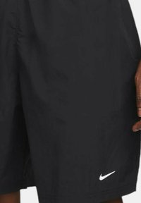Black Nike shorts with a relaxed fit, made of lightweight fabric. Features a white logo on the lower hem and a smooth texture.