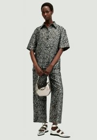 Koszula i spodnie w panterkę w odcieniach szaro-czarnych. Gładki materiał, krótki rękaw i kołnierzyk. Trzyma srebrną torebkę. Srebrne buty.