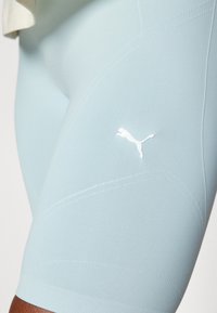 Nahaufnahme von hellblauen Sportshorts mit weißem Puma-Logo am Oberschenkel, getragen von einer Person mit dunkler Hautfarbe.