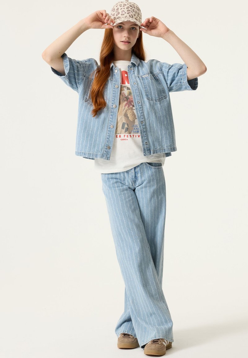 Tenue en denim bleu clair avec un motif rayé. Comprend une veste à manches courtes, un pantalon large assorti et une casquette beige à imprimé léopard.