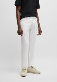 Valged puuvillased püksid, slim fit lõikega, koos klassikalise viie tasku disainiga ja peente õmbluse detailidega. Kombineeritud beežide spordijalatsitega.