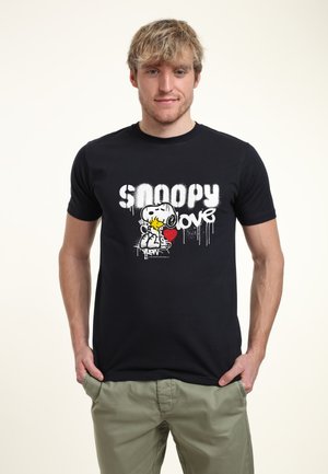 Giovane con capelli biondi che indossa una t-shirt nera con la grafica di Snoopy e Woodstock e le parole "Snoopy Love" in bianco.