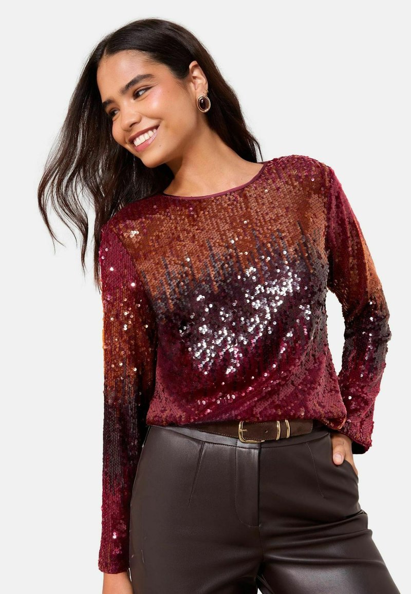 Burgundijas krāsas garām piedurknēm topiņš ar pērlītēm, kura gradienta tonis ir no tumšāka uz gaišāku, kombinēts ar pieguļošām brūnām ādas biksēm un jostu.