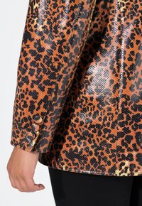 Leopardmönstrad blazer med glänsande, strukturerat material. Har svart och orange mönster, tre knappar på ärmslutet och skräddarsydd passform.