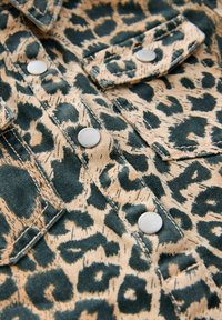 Tkanina s leopardím vzorom v zelenej a béžovej farbe s kovovými striebornými cvokmi a detailným prešitím. Vyznačuje sa textúrovaným, tkaným povrchom.