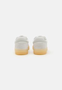 Hvite semskede sneakers med en glatt tekstur, rund fasong, gummisåler og minimalistisk design. Bakfra viser de sømdetaljer.