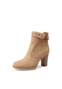 Stivaletto alla caviglia in suede beige con design perforato ai lati, punta tonda e tacco a blocco. Decorato con borchie e dettaglio della fibbia.