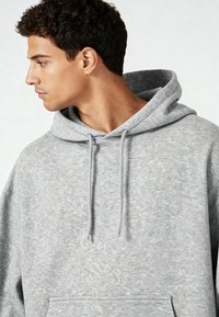 Grauer Pullover-Hoodie aus weichem Material, ausgestattet mit einer Kordelzugkapuze, einer Kängurutasche und einem lässigen Schnitt mit leicht strukturierter Oberfläche.