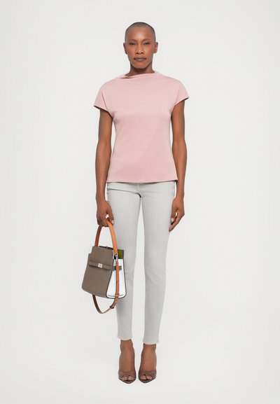 Ljusrosa kortärmad topp som är ihopparad med grå slim-fit-byxor. Modellen håller en strukturerad brun och vit handväska med ett orange band.