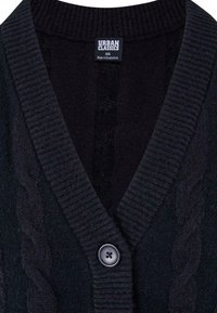Cardigan noir en maille tricotée avec un col en V, une texture côtelée et un motif torsadé, terminé par un bouton noir unique au niveau de l'encolure.