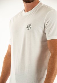 T-shirt bianco in cotone con scollo rotondo e maniche corte, dotato di un piccolo logo ricamato in nero sulla parte sinistra del petto.