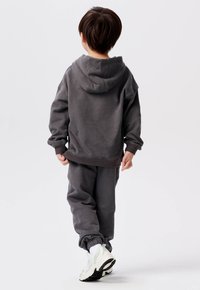 Grijze hoodie en sweatpants set van zachte stof, met een relaxte pasvorm en ribbelboorden. Vergezeld van witte en lichtgrijze sport sneakers.