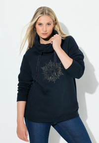 Sudadera azul marino con cuello tipo cowl, que presenta un diseño de copo de nieve plateado y cordones más oscuros. Tejido suave y corte relajado.