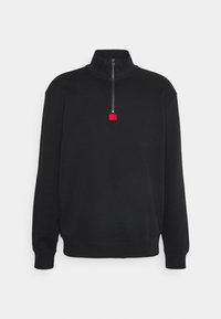 Sort sweatshirt med lynlås og høj hals lavet af blødt stof. Den har en stående krave, lange ærmer og en lille rød logo på brystet.