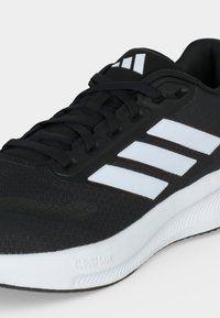 Schwarz-weißer Sportschuh mit schwarzen Schnürsenkeln, weißen Adidas drei Streifen an der Seite und einer weißen gepolsterten Sohle mit der Bezeichnung Cloudfoam.