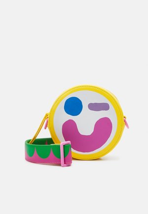 Sac bandoulière rond jaune avec un motif abstrait coloré de visage et une sangle réglable verte et rose.