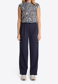 Granatowe spodnie z wysokim stanem i szerokimi nogawkami w połączeniu z przezroczystą bluzką w czarno-biały wzór zebry. Teksturowany materiał, swobodny styl.