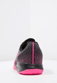 Musta urheilujalkine, jossa on vaaleanpunaisia yksityiskohtia, teksturoitu päällinen, pehmustettu nilkkakaulus ja vaaleanpunainen kumipohja, jossa on sahalaitainen kuvio.