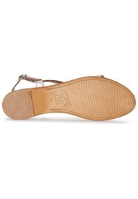 Sandale marron avec une semelle plate, une sangle de cheville ajustable et une semelle extérieure en caoutchouc texturé. Des accents métalliques ornent la sangle supérieure.