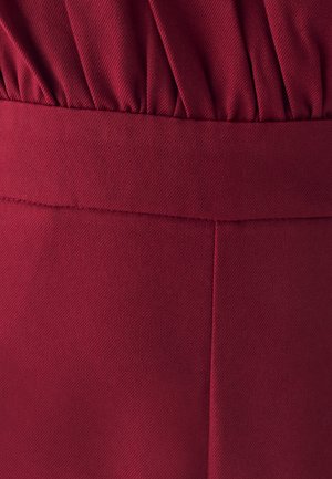 Tela burdeos con un patrón texturizado y acanalado; cuenta con una cinturilla fruncida y un acabado suave con detalles de costura visibles.