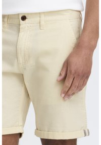 Beige shorts van een lichtgewicht stof, met een knoopsluiting, zijzakken en manchetten met gestreepte accenten.