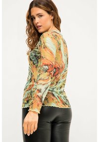 Langärmeliges, leichtes Oberteil mit einem mehrfarbigen, abstrakten Muster in Grün, Orange und Braun. Enganliegendes Design mit gewelltem Saum.
