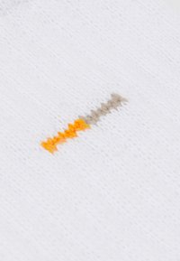 Tissu tricoté blanc avec une surface texturée présentant des motifs en zigzag aux couleurs orange, beige et gris au centre.