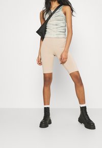 Tank-Top in grün-beige Tie-Dye, kombiniert mit beigen Radshorts. Schwarze Combat Boots mit dickem Sohlen. Schwarze Umhängetasche.