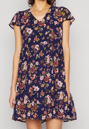 Woman wearing a navy blue short-sleeve dress with pink, red, and orange floral print and a V-neckline.