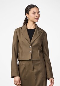 Blazer brun coupé avec un col cranté, deux boutons et des manches longues. Le tissu a une texture lisse, jupe ajustée assortie visible.