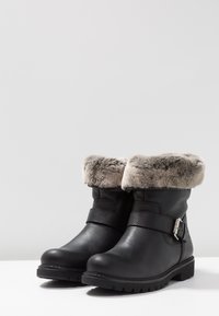 Black leather ankle boots with a gray fur cuff, featuring a decorative strap with a silver buckle and textured rubber sole.