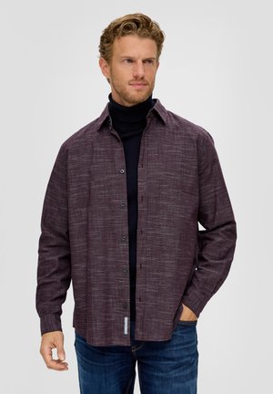 Bordeauxfarbiges Hemd mit Knopfverschluss aus einem strukturierten Stoff, entspannter Schnitt, spitzem Kragen und Brusttasche. Getragen über einem schwarzen Rollkragenpullover.