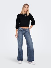 Black cropped sweater with a textured finish, high-waisted blue flared jeans, and white sneakers. Simple design with basic hardware details.