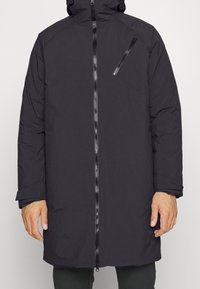 Svart vadderad jacka med huva, framsida med dragkedja och sidofickor. Den har en elegant design med en texturerad tyg och skräddarsydd passform.