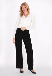 Cardigan alb tricotat cu decolteu zimțat și nasturi, asortat cu pantaloni negri cu croială largă și tocuri negre ascuțite.