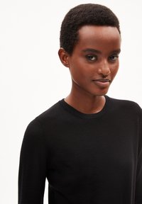 Schwarzer Strickpullover mit Rundhalsausschnitt und langen Ärmeln. Die Textur ist glatt und leicht tailliert, mit minimalen Details.