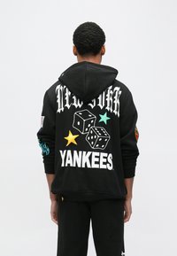 Czarna bluza z kapturem z białymi napisami "NEW YORK" i "YANKEES". Ozdobiona kolorowymi gwiazdkami i grafikami kości do gry. Miękka w dotyku, o swobodnym kroju.