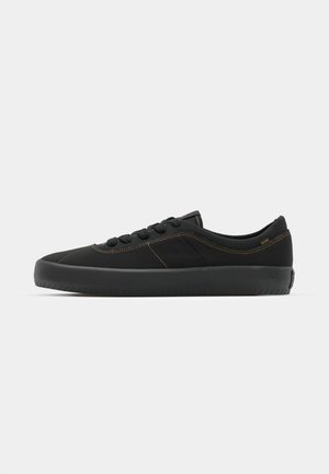 Black sneaker with a smooth textile upper, contrasting brown stitching, round toe, lace closure, and a thick rubber sole for traction.