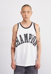 Balta akių topas su užrašu „CHAMPION“ storomis juodomis raidėmis, su juodu kampu ir šoniu. Pilki džinsiniai šortai.