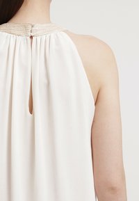 Robe blanche avec une bordure métallique tissée au niveau de l'encolure, présentant une ouverture en trou de serrure au dos et un tissu doux et léger.